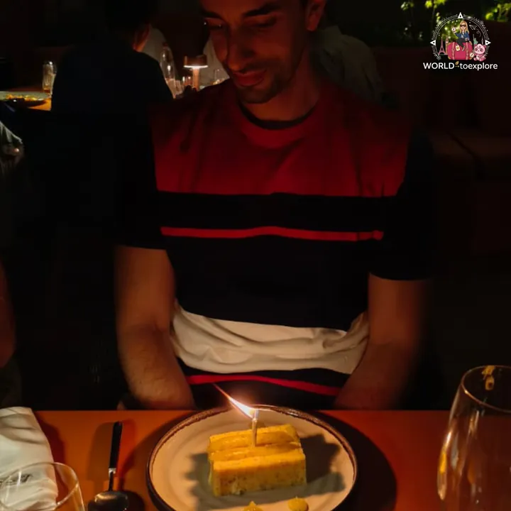 The birthday boy looking at the slice of cake with a lit candle, at the happy birthday moment, at night