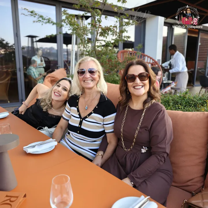 Three women seated at the table on the RENATA terrace, smiling, with the table set and a waiter in the background