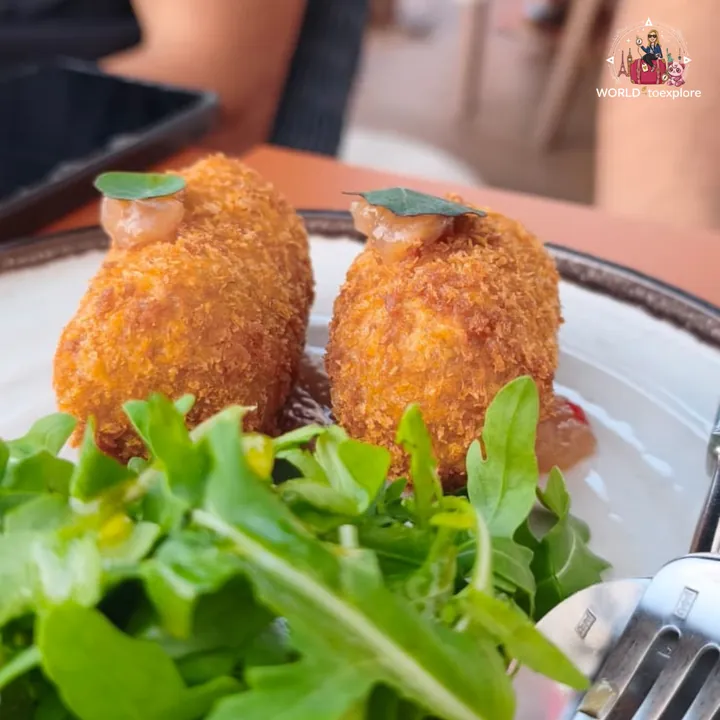 The suckling pig croquettes, golden and crispy, topped with a leaf and served with rocket