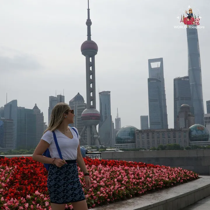 The author walking past a flower bed on the Bund, with the Oriental Pearl and the Shanghai Tower in the background