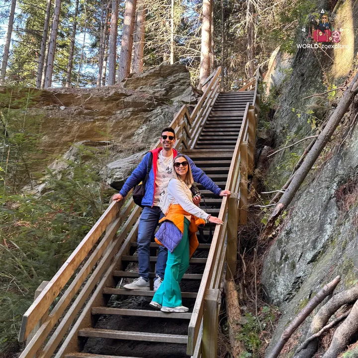 A smiling couple on a wooden staircase along the Tiki Trail, built against a rock wall