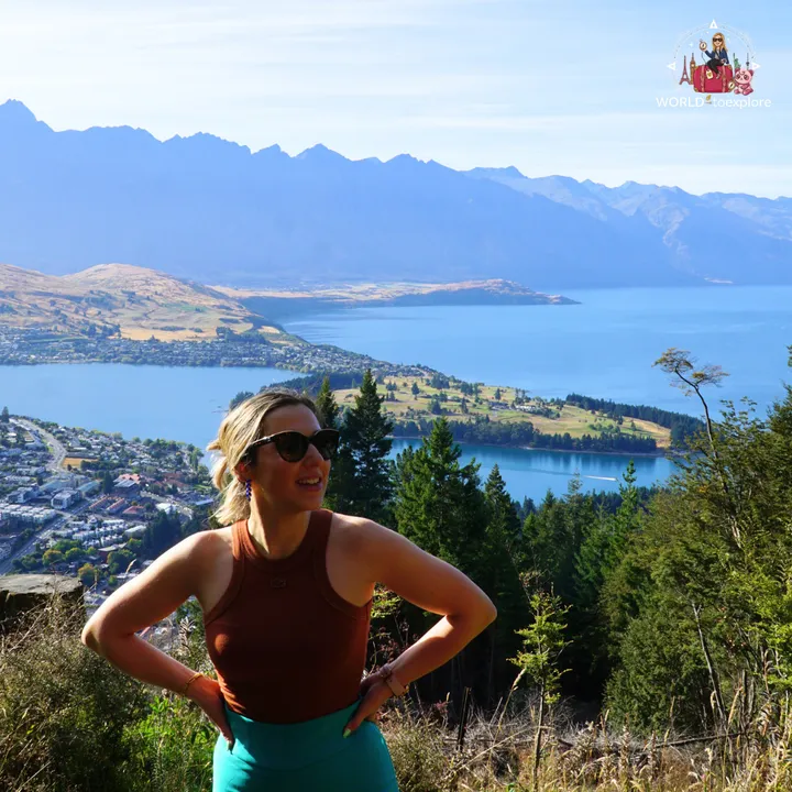 The author smiling with her hands on her hips, with Lake Wakatipu and the Queenstown mountains in the background