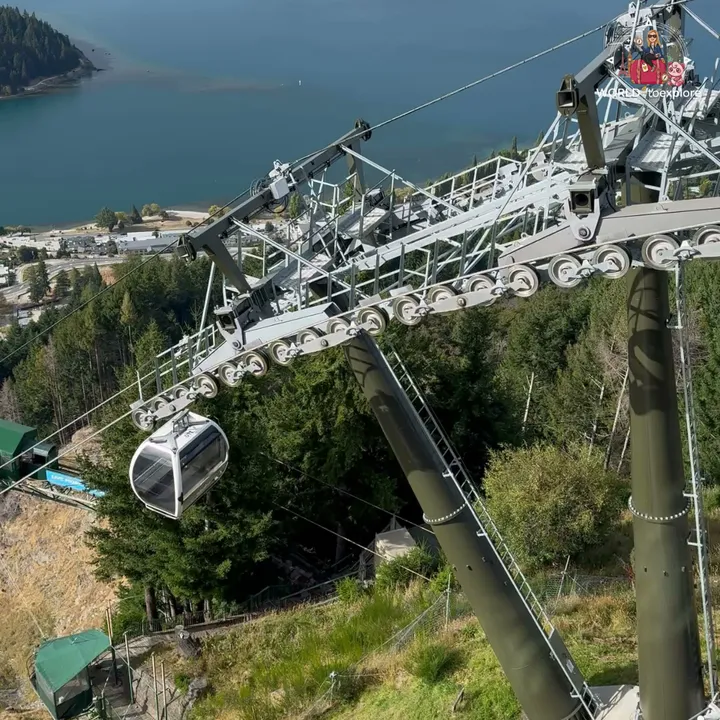 Support structure of the Skyline Gondola with a cabin passing by, with Lake Wakatipu and the town in the background