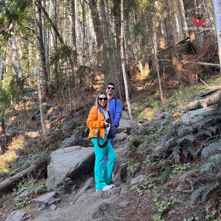 A smiling couple posing on a rock in the middle of the Tiki Trail, surrounded by ferns and trees