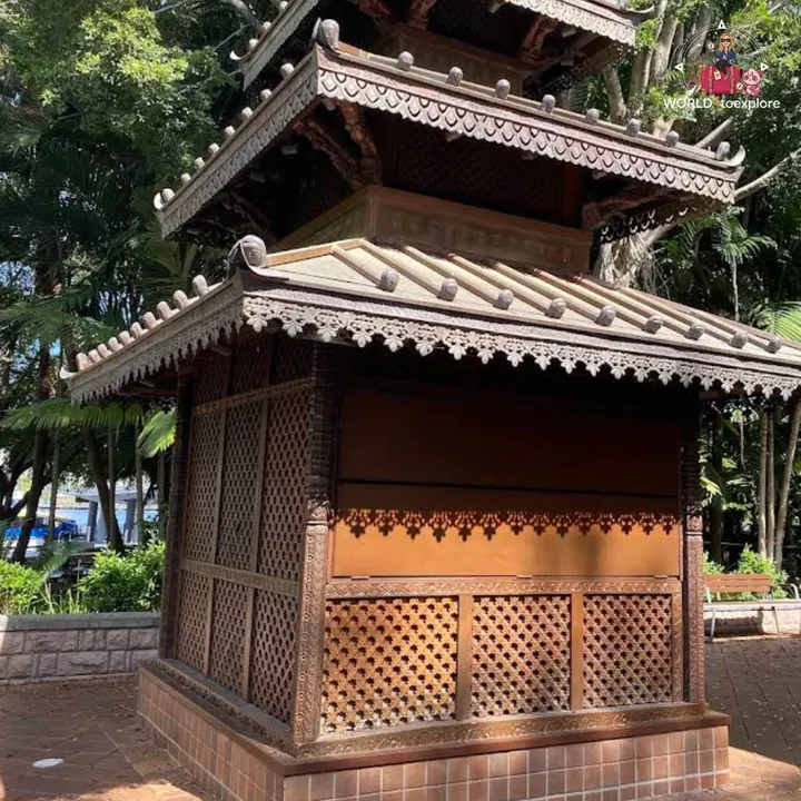 The Nepal Peace Pagoda seen from the side, with its tiered roofs and wood carvings, surrounded by trees