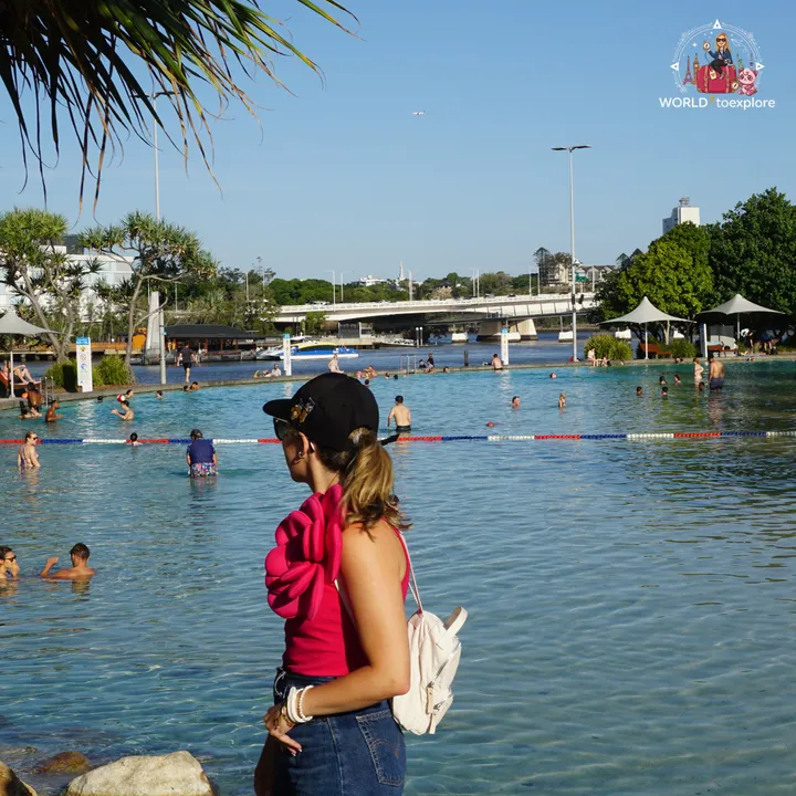 Looking out over the Streets Beach lagoon, with people swimming, palm trees and a bridge over the river in the background
