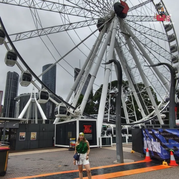 Posing in front of the Wheel of Brisbane, the South Bank observation wheel, on a cloudy day, with the skyscrapers behind