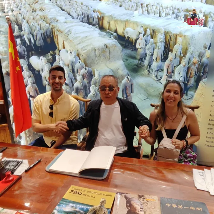 The couple shaking hands with a man at a book stand about the Terracotta Army, with the Chinese flag