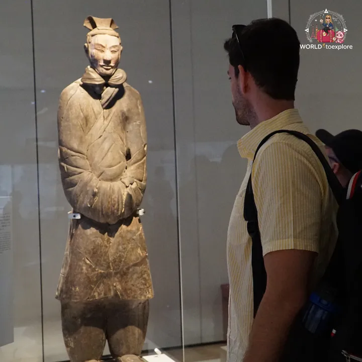 Terracotta warrior on display in a museum case, watched by a visitor