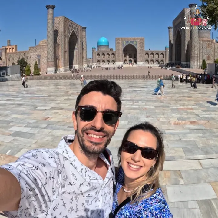 Couple taking a selfie in Registan Square, in Samarkand, with the blue-tiled madrasas in the background