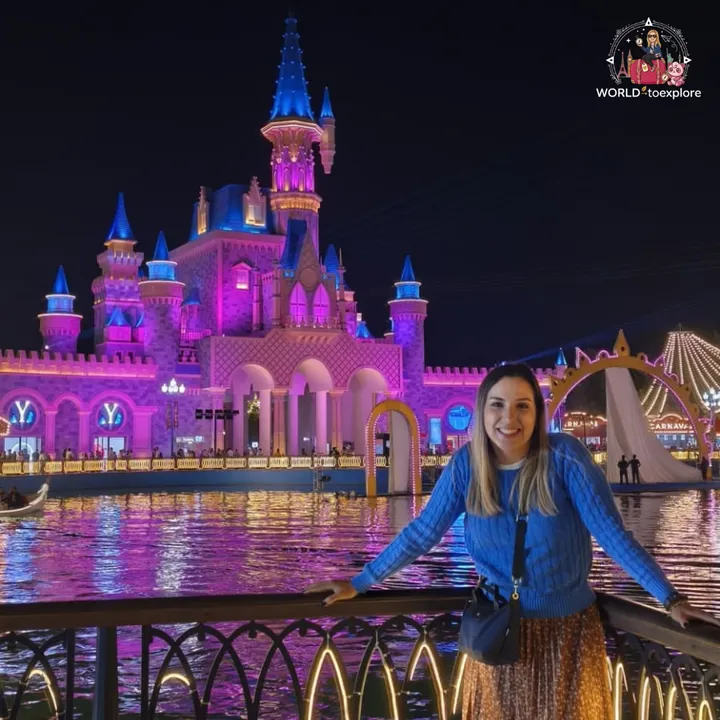 Smiling woman by a lake, with a castle lit up in purple and blue at a night attraction in Tashkent