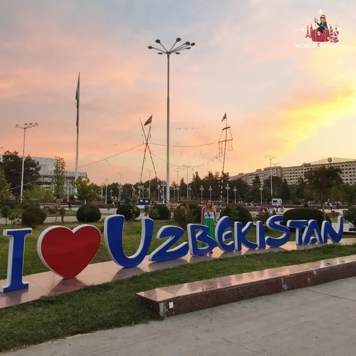 Woman next to a three-dimensional sign reading I love Uzbekistan, in a park at sunset