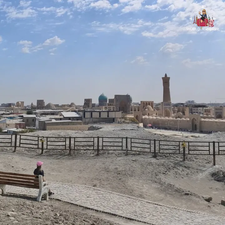 View over the Bukhara skyline, with the Kalyan Minaret and several historic domes, and a bench in the foreground